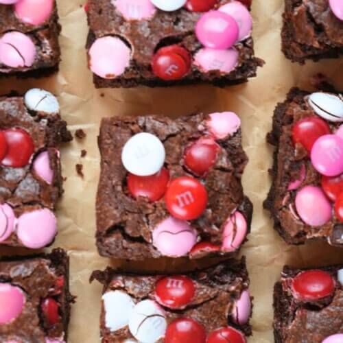 Cut squares of sourdough Valentine's brownies topped with colorful M&M's, arranged on parchment paper