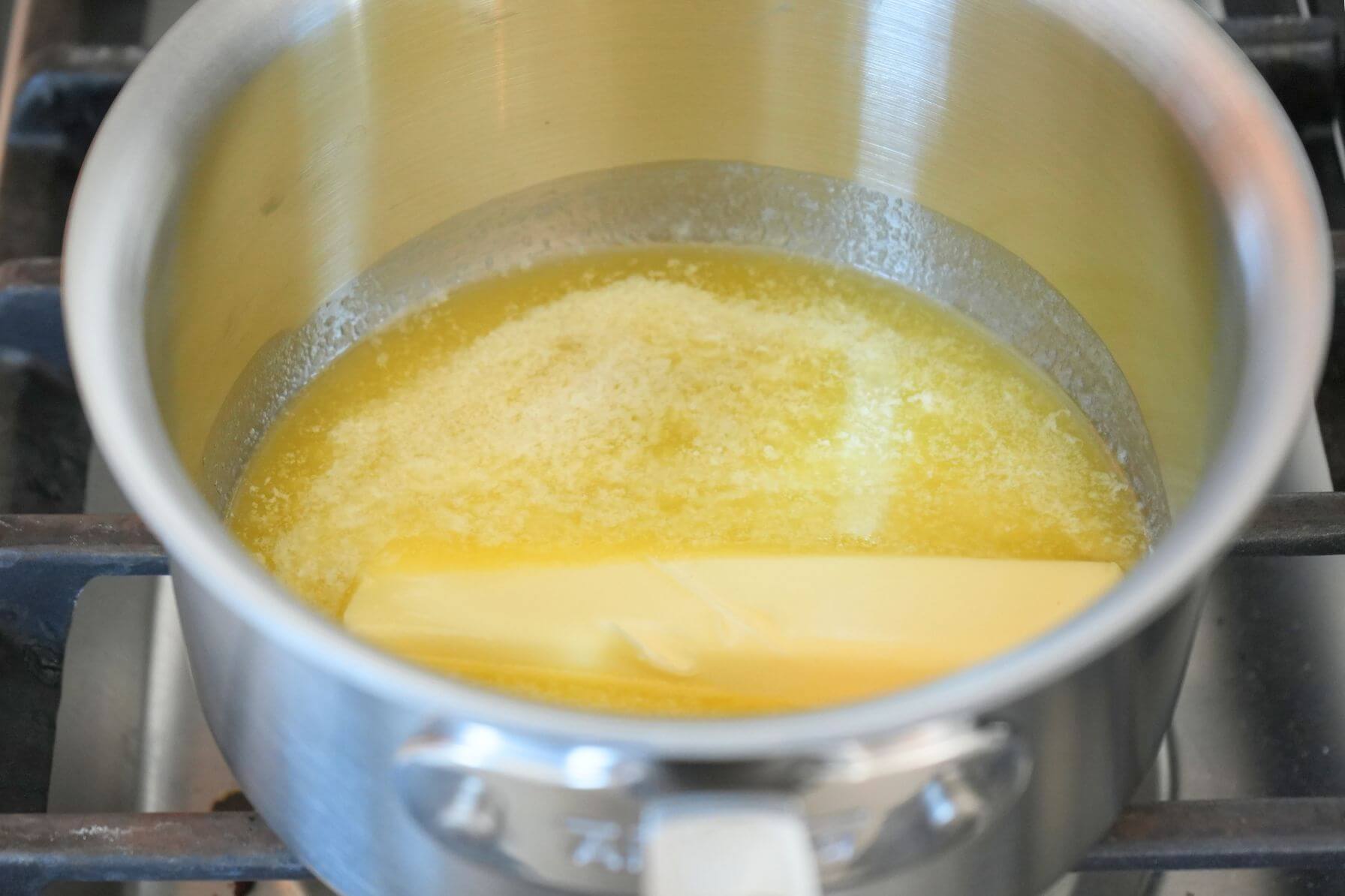 A saucepan on the stove with a stick of butter melting.