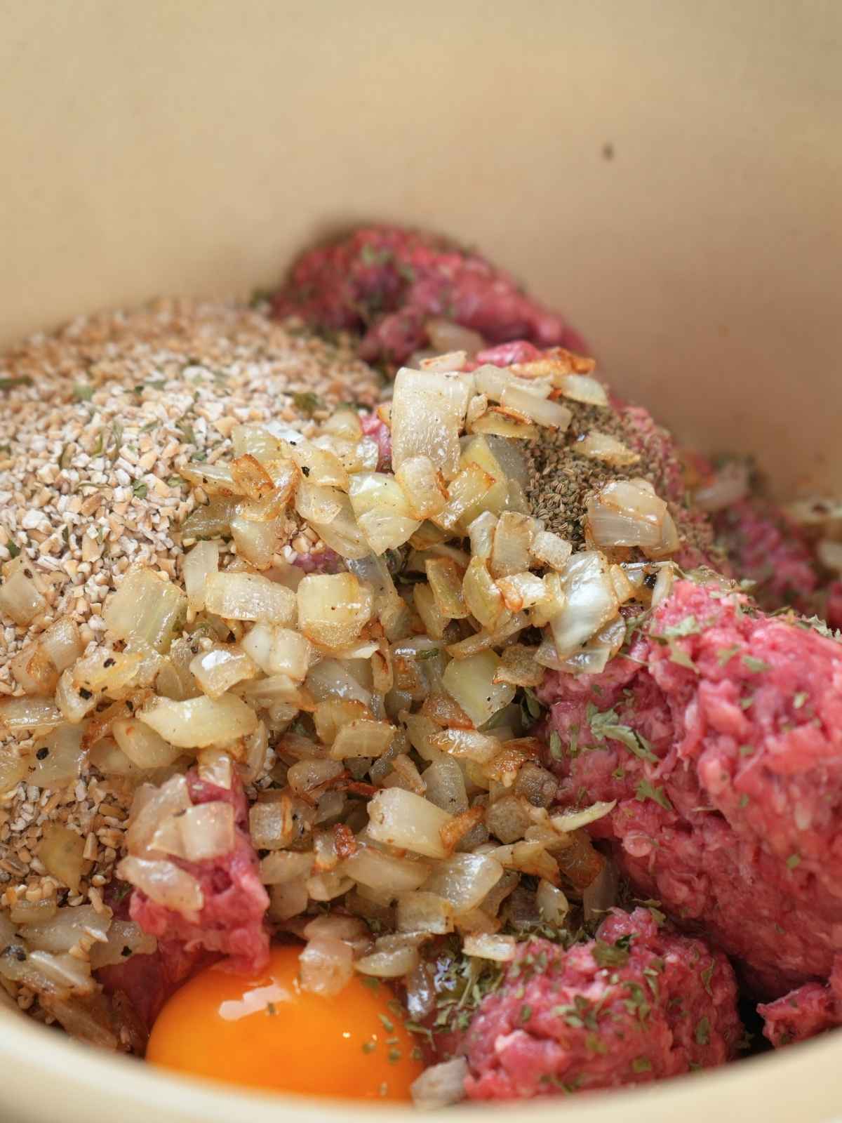 Mixing bowl filled with ground beef, sautéed onions, steel-cut oats, eggs, and seasonings for the meatloaf mixture.