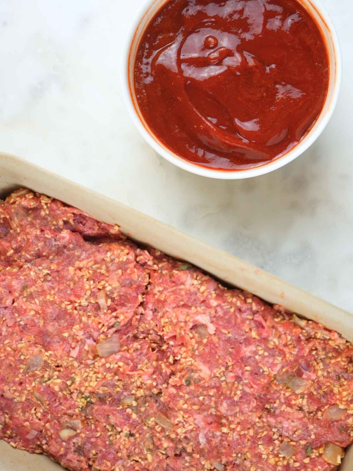 Bowl of hot honey sauce placed next to the uncooked meatloaf in a baking dish.