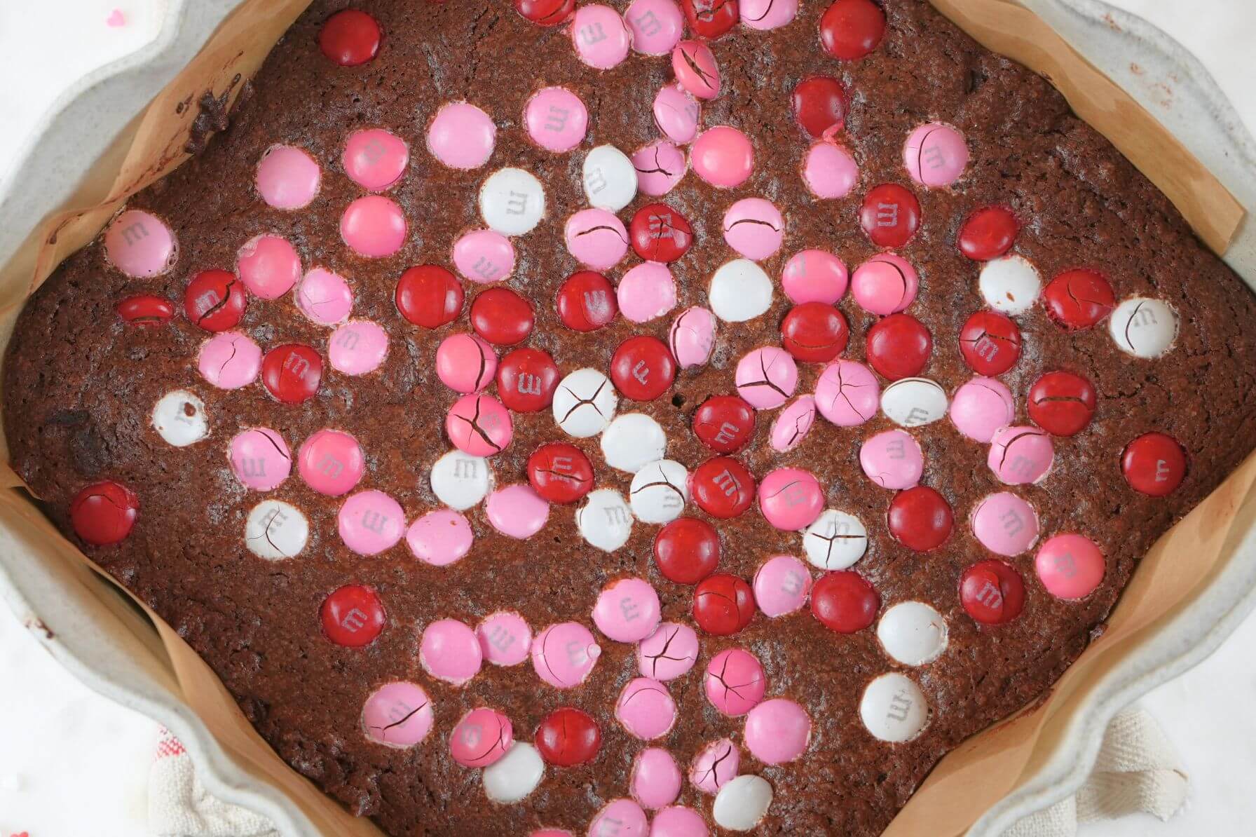 Sourdough Valentine's brownies in a baking dish, topped with cracked pink, red, and white M&M's.
