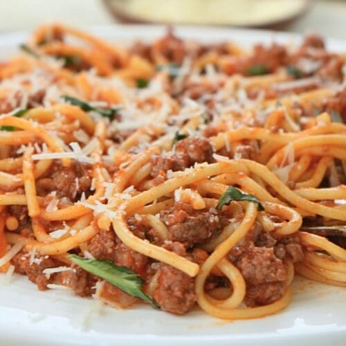 Close-up of spaghetti with meat sauce, basil, and parmesan on a white plate.