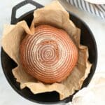 Freshly baked einkorn sourdough bread in a Dutch oven lined with parchment paper.