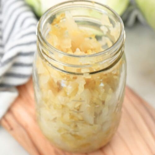 A mason jar filled with homemade sauerkraut shown with a decorative towel