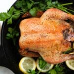 Roast chicken garnished with parsley and lemon slices, served in a cast-iron skillet