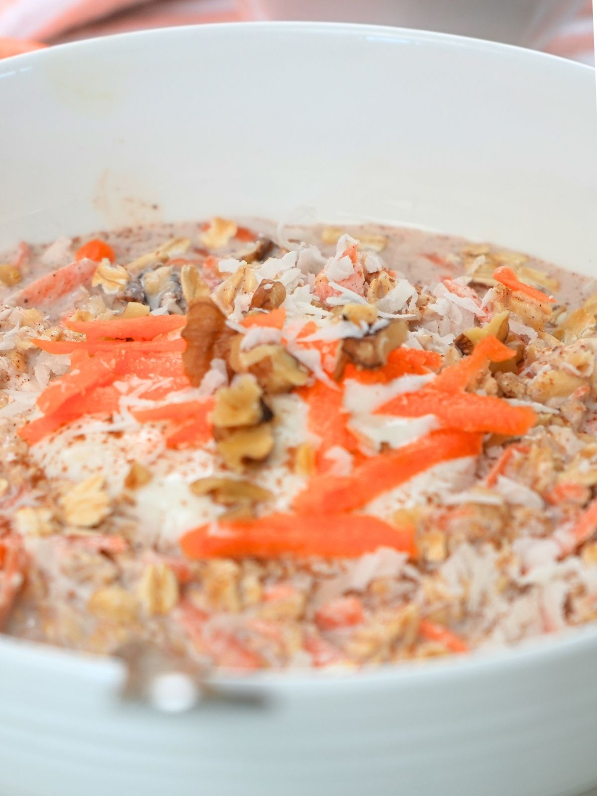 Carrot cake overnight oats in a white bowl topped with yogurt, coconut, shredded carrots, and coconut.