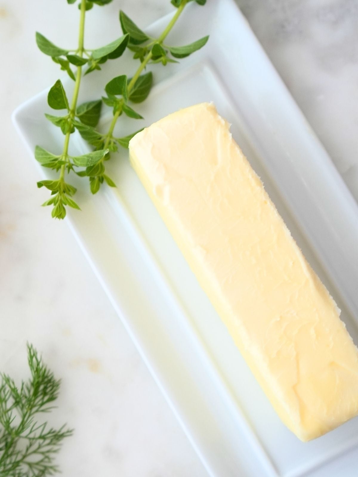 A stick of butter next to fresh herbs.