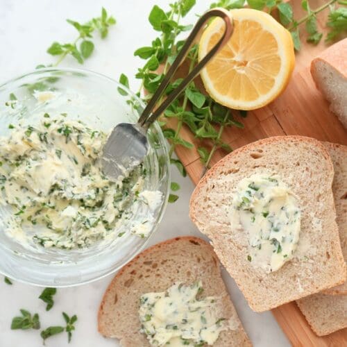 Herb butter in a bowl and on bread, next to a fresh lemon and herbs.