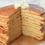 A stack of sourdough discard pancakes topped with butter and a wedge cut out.