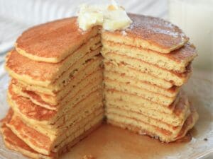 A stack of sourdough discard pancakes topped with butter and a wedge cut out.