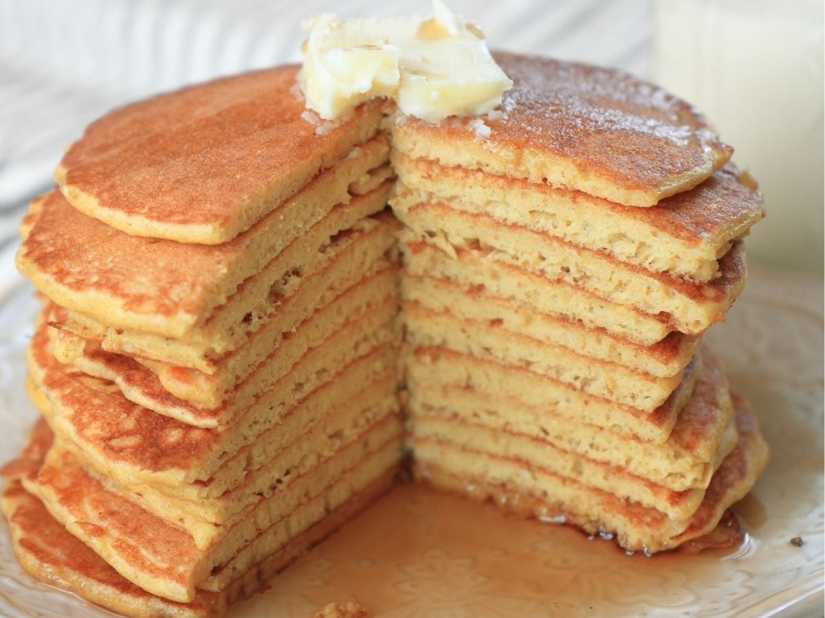 A stack of sourdough discard pancakes topped with butter and a wedge cut out.