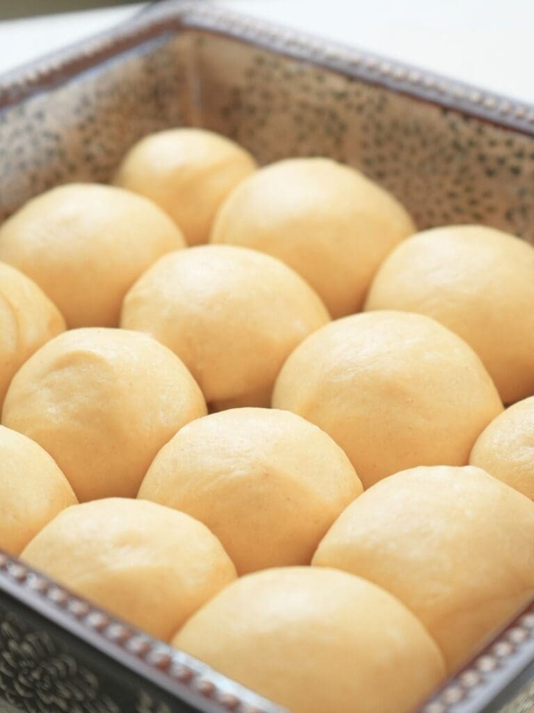 Sourdough brioche rolls arranged in a square baking dish.