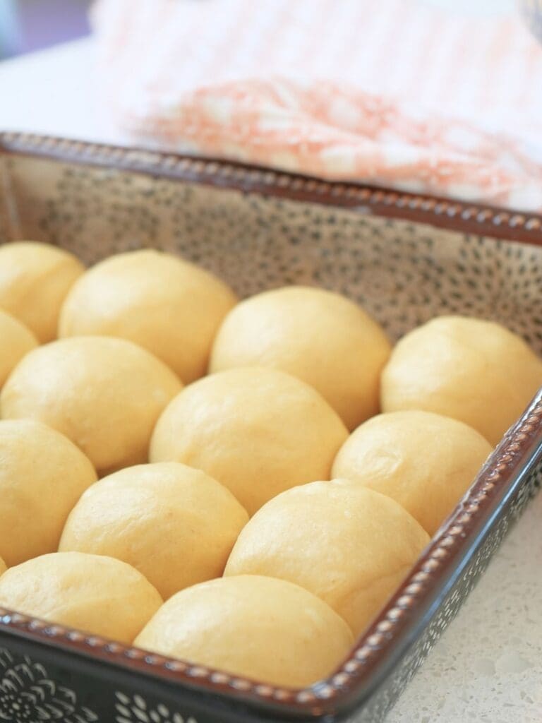 Unbaked rolls in a baking dish, shown next to a towel for covering.