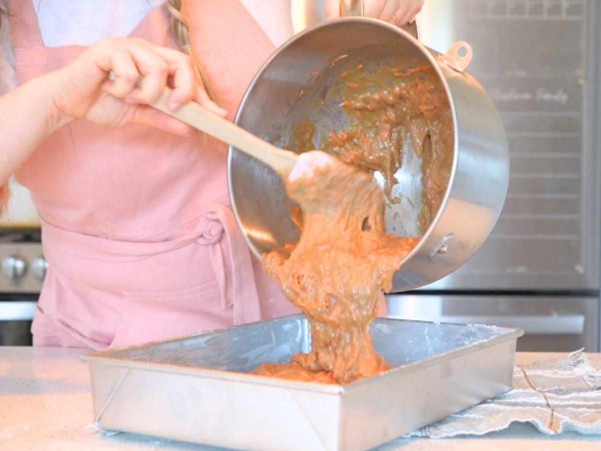 Woman pouring sourdough carrot cake batter into a cake pan.