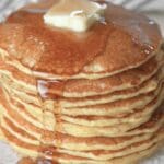 Stack of sourdough discard pancakes topped with butter and drizzled with maple syrup.