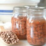 Jars of home-canned pinto beans shown with a wood scoop of dried beans and a mixing bowl in the background