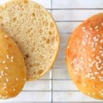 Two sourdough burger buns resting on a wire cooling rack, one cut open