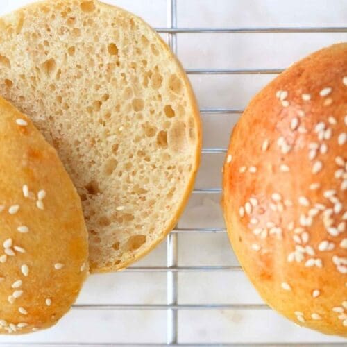 Two sourdough burger buns resting on a wire cooling rack, one cut open