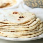 A stack of sourdough discard tortillas on a plate with a decorative bowl in the background.