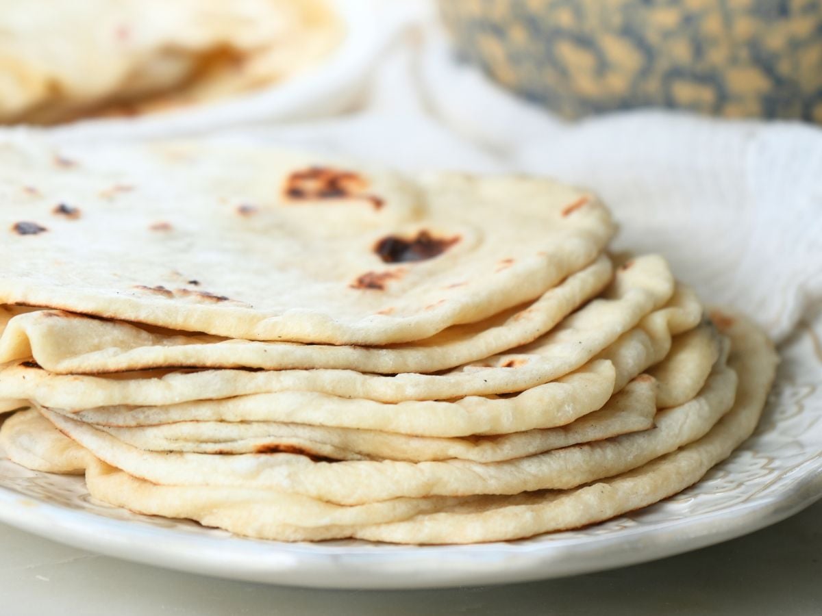 A stack of sourdough discard tortillas on a plate with a decorative bowl in the background.