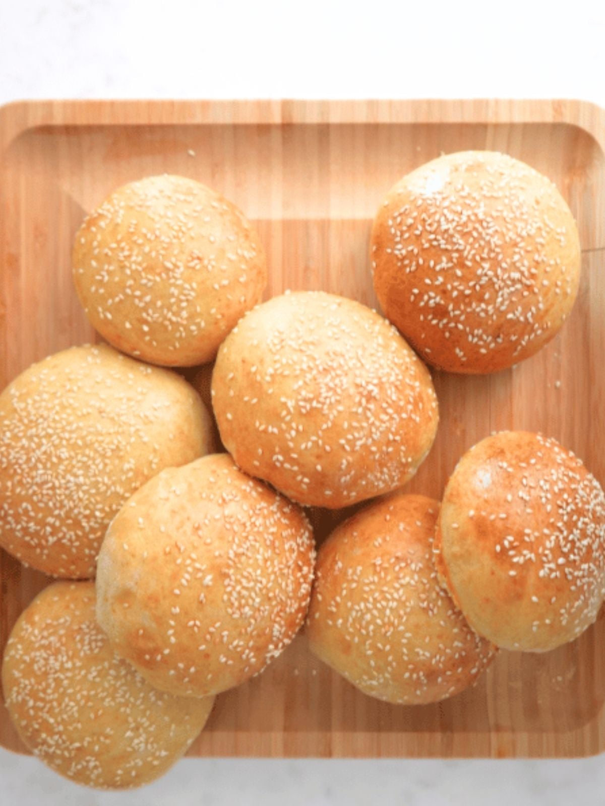 Sourdough burger buns piled on a wooden board.