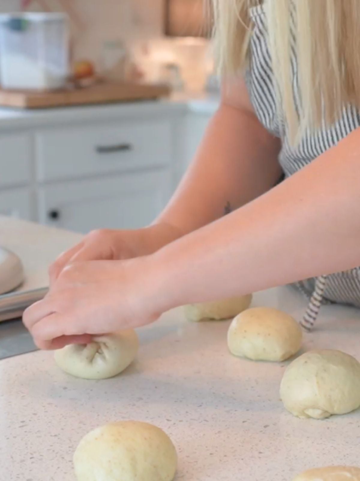 Woman shaping sourdough buns on countertop.