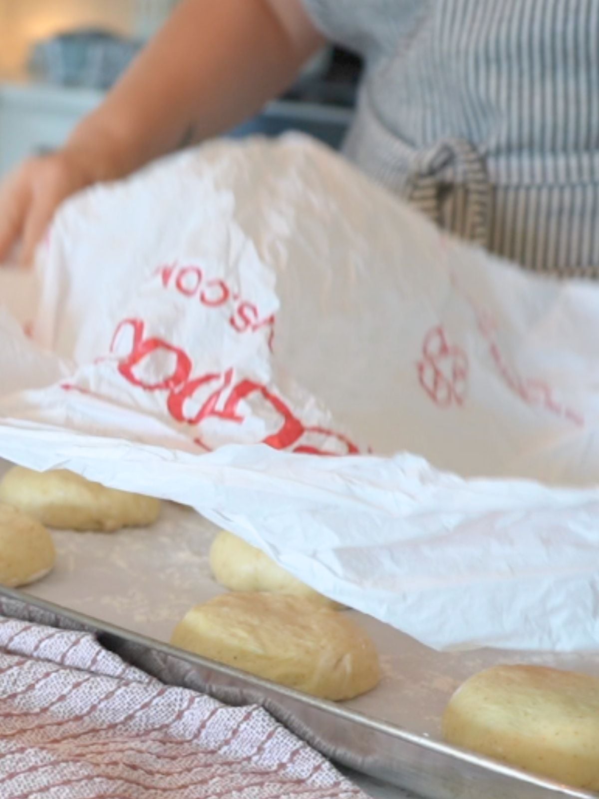 Woman covering sourdough burger bun dough with plastic.