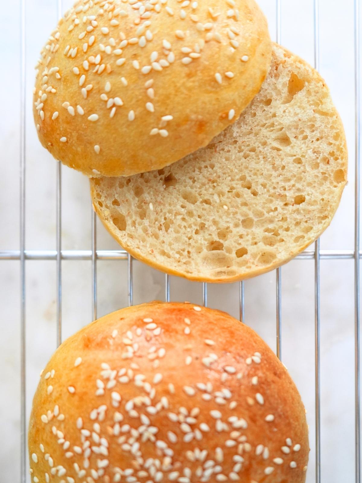 Two sourdough burger buns on a cooling rack, one sliced open.