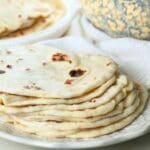 A stack of sourdough discard tortillas on a plate with a decorative bowl in the background