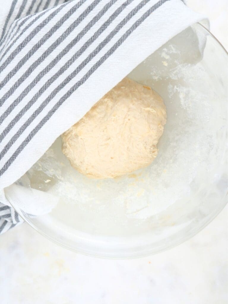 Sourdough discard tortilla dough in a bowl, partially covered with a towel.