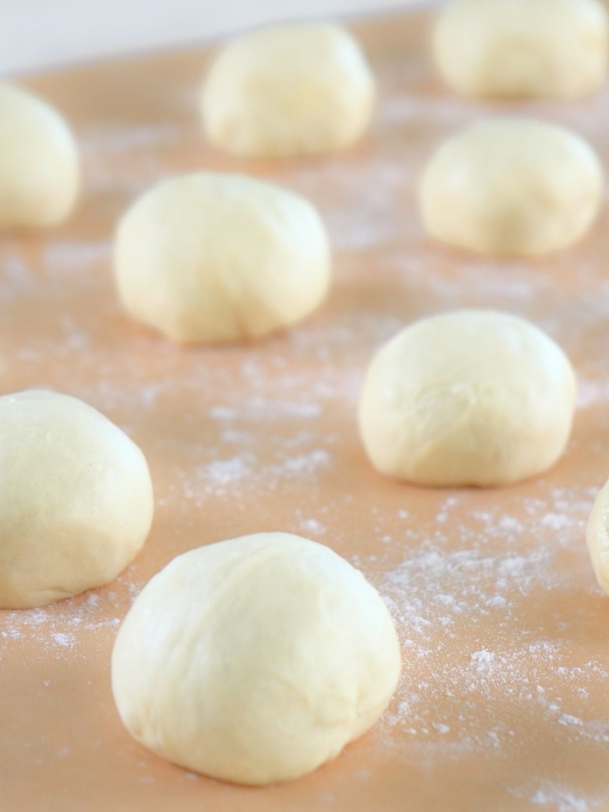 Dough shaped into balls and resting on a piece of floured parchment paper.
