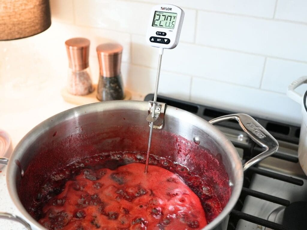 Strawberry jam ingredients in a stock pot with a candy thermometer reading 220 degrees.