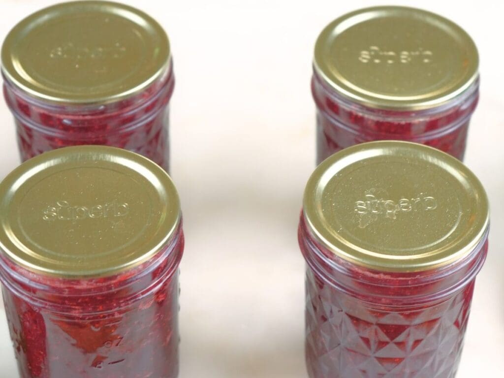 Jar of canned strawberry jam resting on a counter.