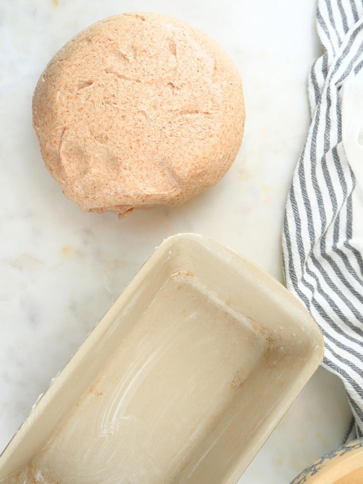 Dough on a counter and a buttered loaf pan.