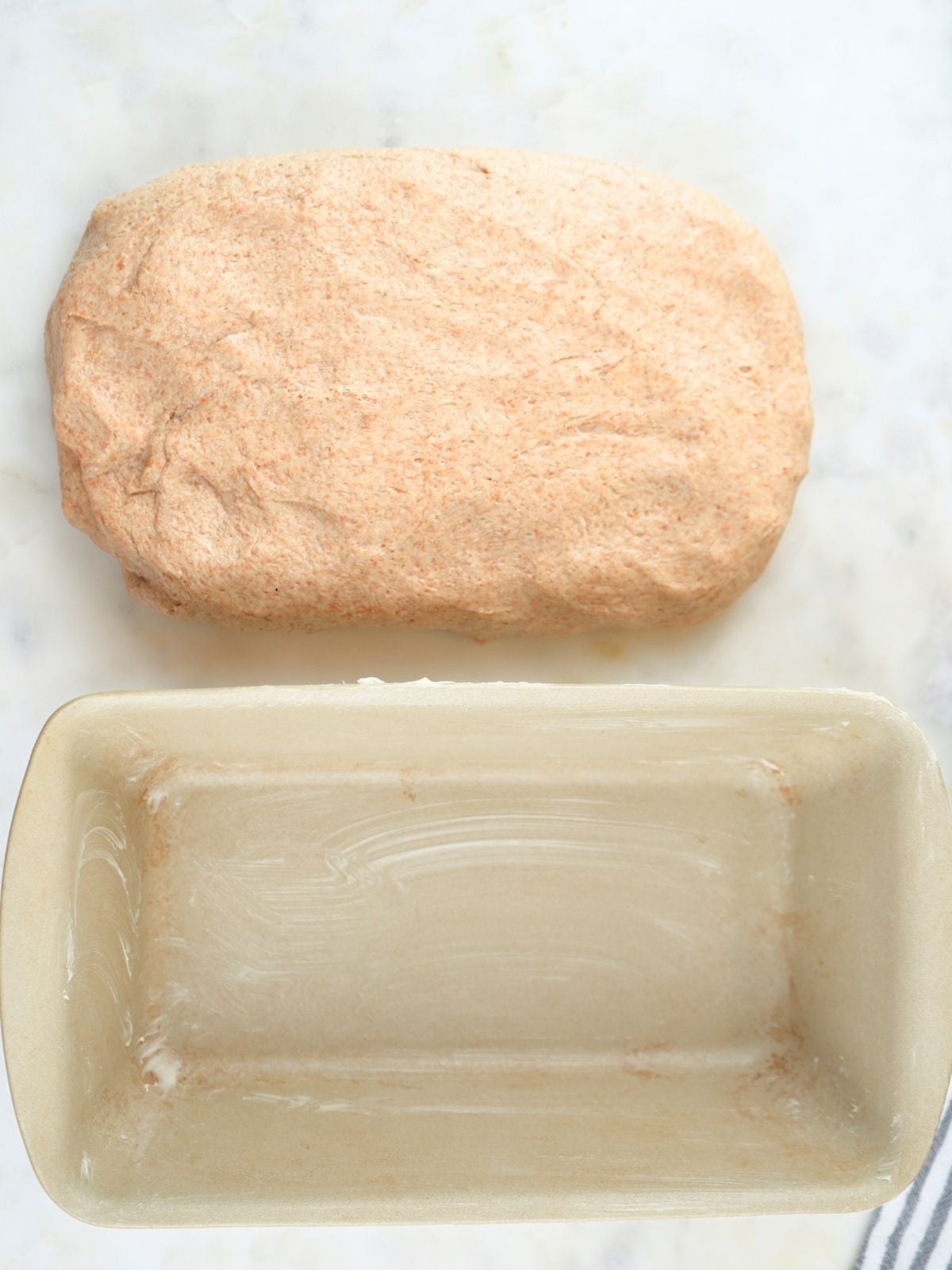 Dough shaped into a rectangle next to a buttered loaf pan.