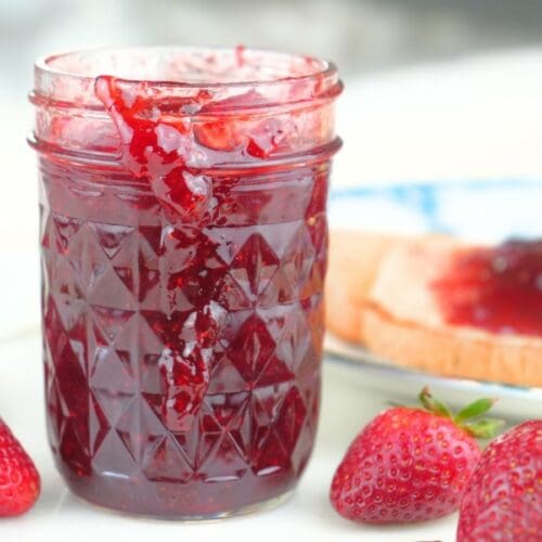 A jar of canned strawberry jam with fresh berries and toast.