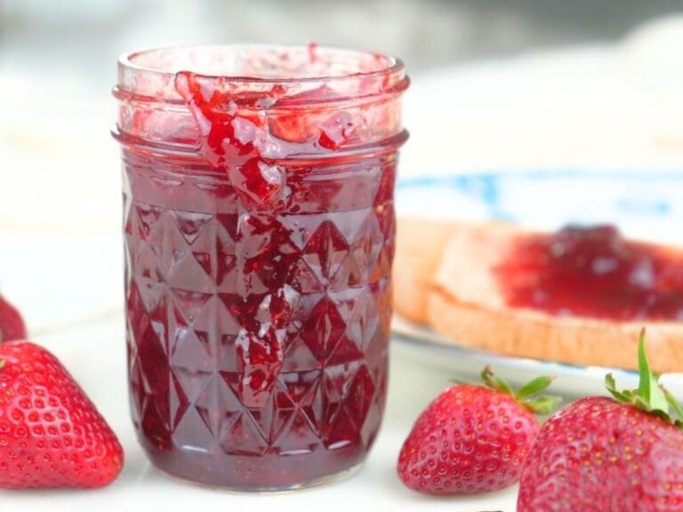 A jar of canned strawberry jam with fresh berries and toast.