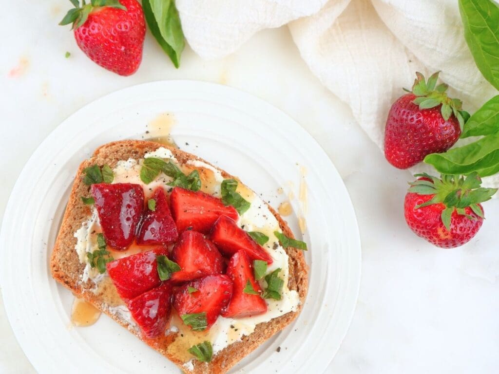 Pickled strawberries on toast with cream cheese and fresh berries scattered.