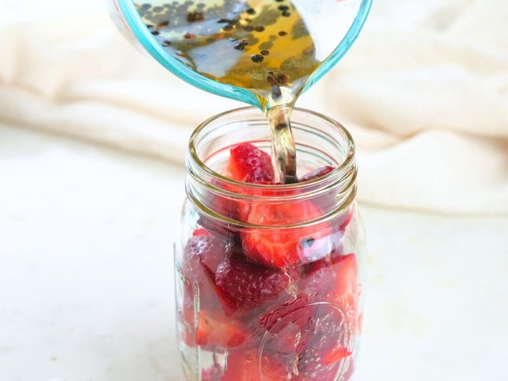 Brine being poured into a jar of fresh strawberries.