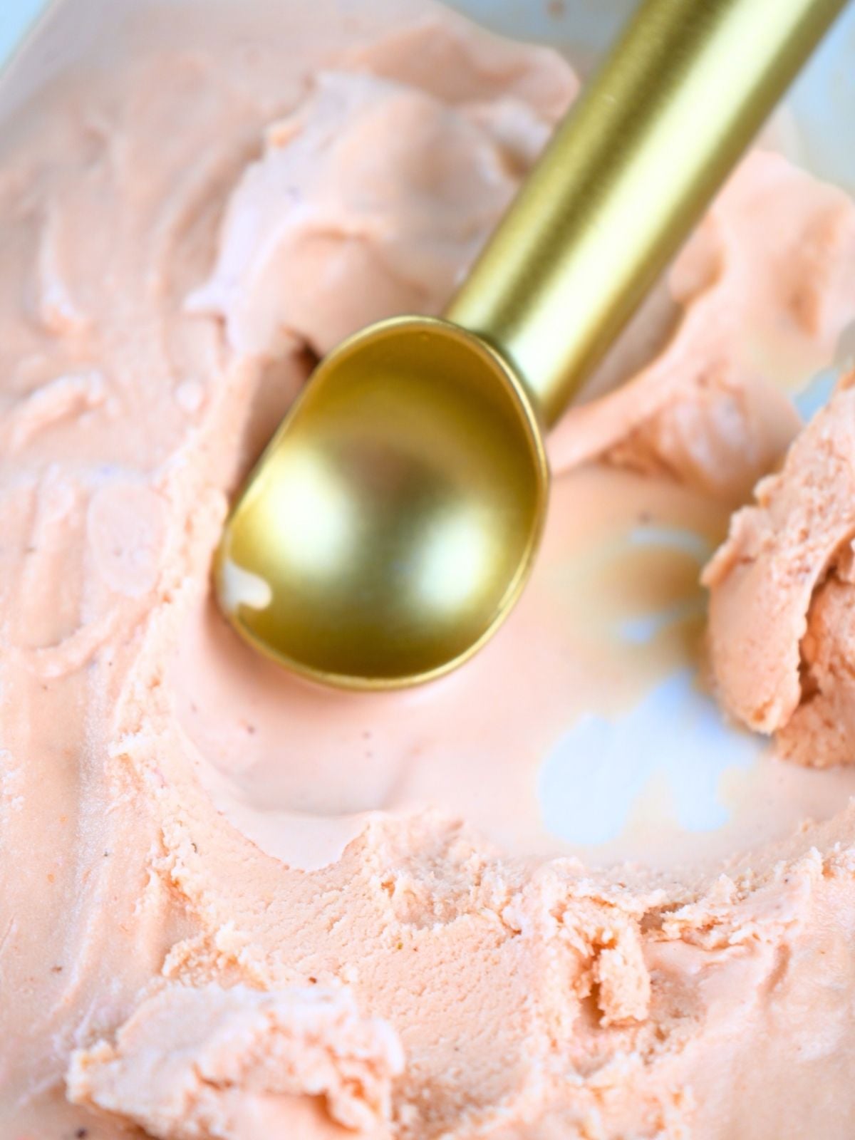 Strawberry ice cream in a dish with a gold scoop.