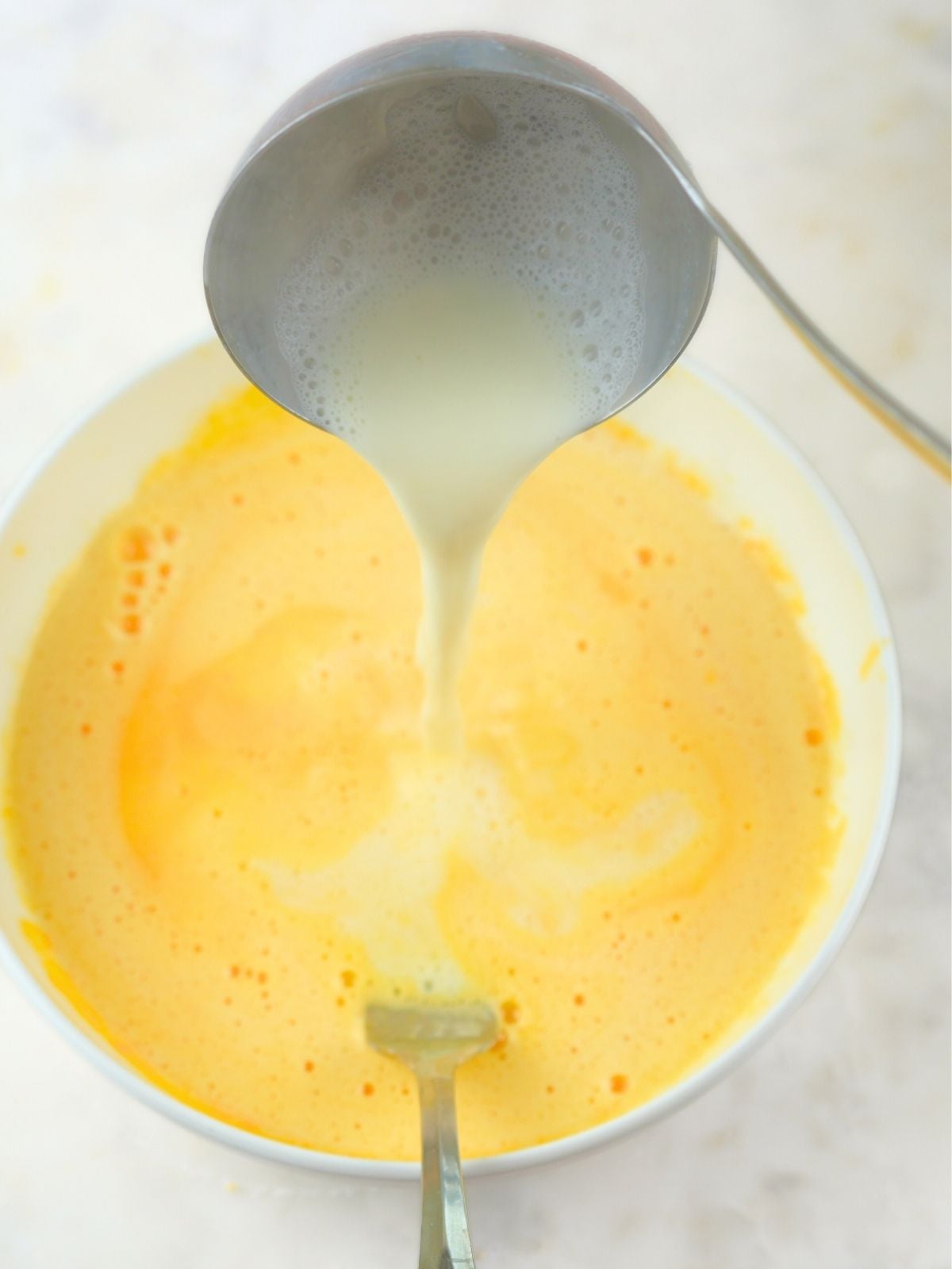 Warm milk mixture being ladled into eggs.