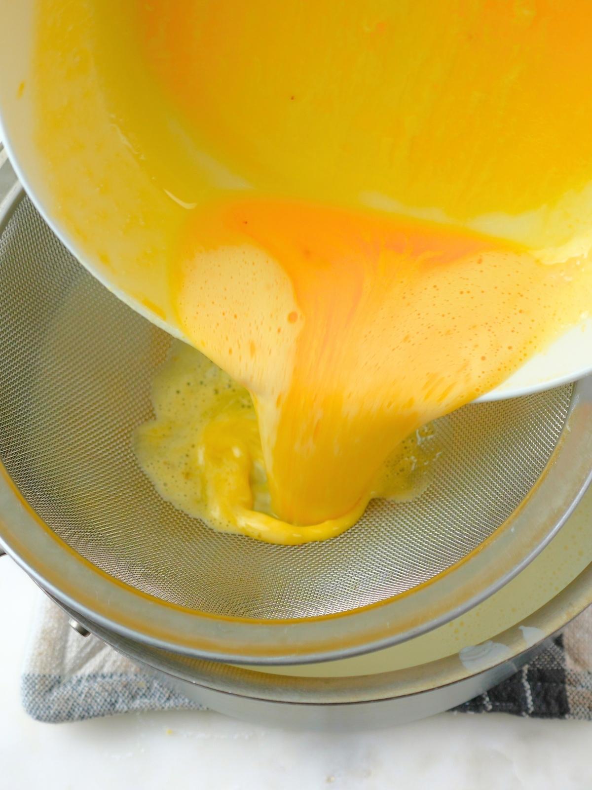 Tempered eggs being poured through a fine mesh strainer.