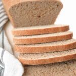Slices of fresh-milled sourdough sandwich bread with a loaf in the background and next to a striped decorative towel