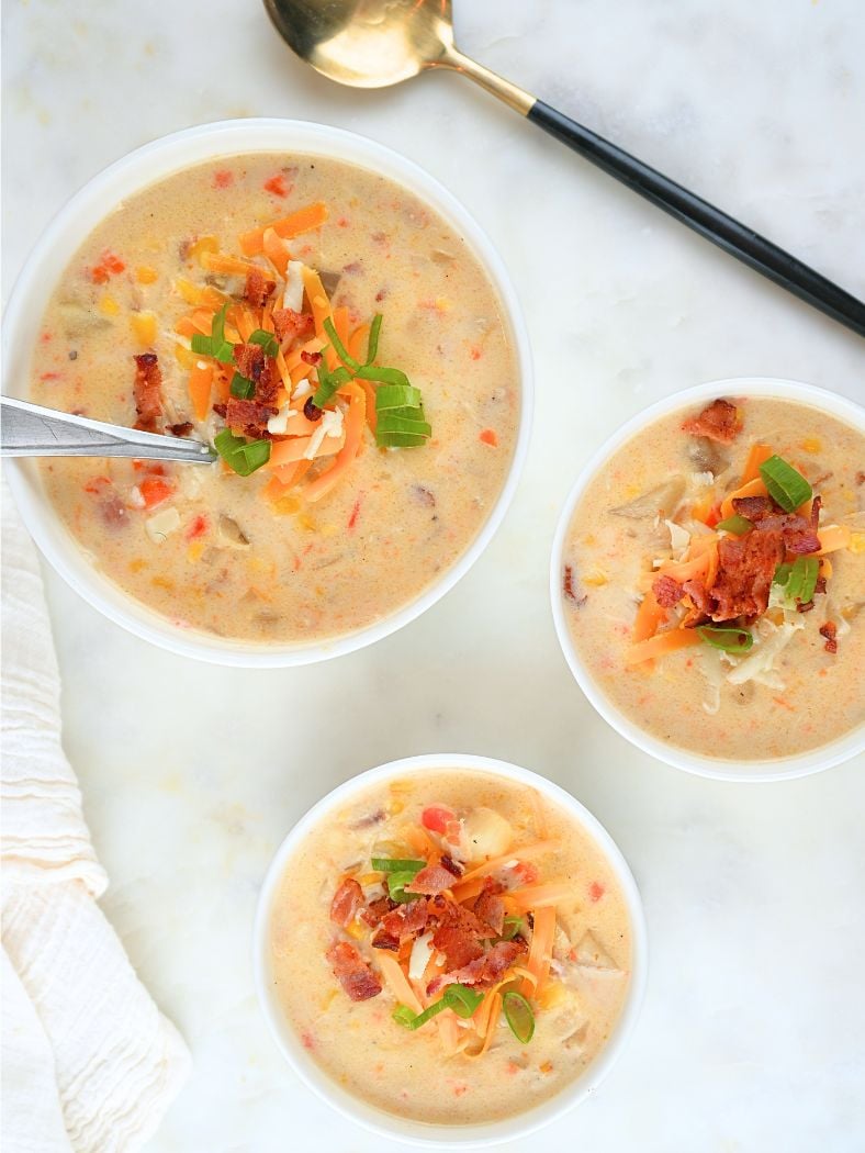 Three bowls of slow cooker chicken corn chowder and a black and gold serving spoon