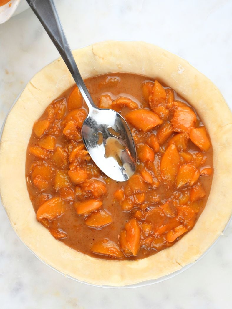 Peach pie filling in a pie dish, shown with a slotted spoon