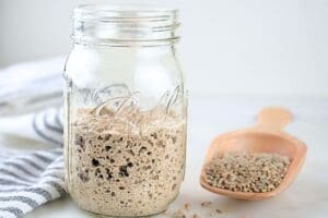 A jar of bubbly fresh-milled flour sourdough starter and a wood scoop of rye berries