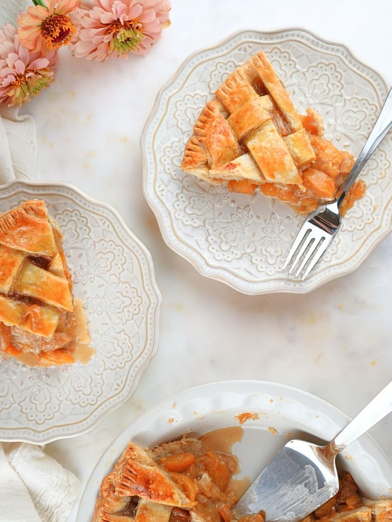Slices of sourdough peach pie on decorative dishes, shown with fresh flowers