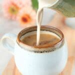 Brown sugar coffee cream being poured into a cup of coffee and flowers in the background