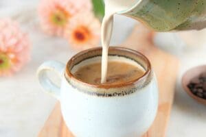 Brown sugar coffee cream being poured into a cup of coffee and flowers in the background