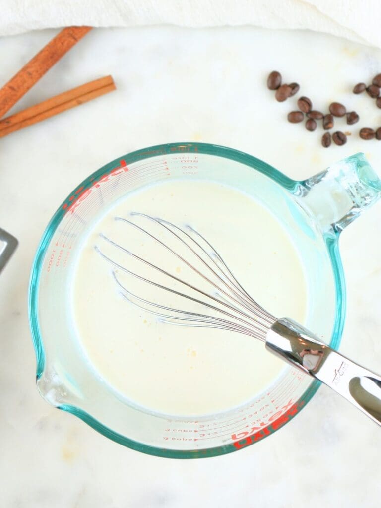 Milk and heavy cream combined in a glass measuring cup with a whisk.